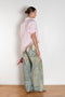 Person wearing a pink shirt and embellished jeans against a white wall.