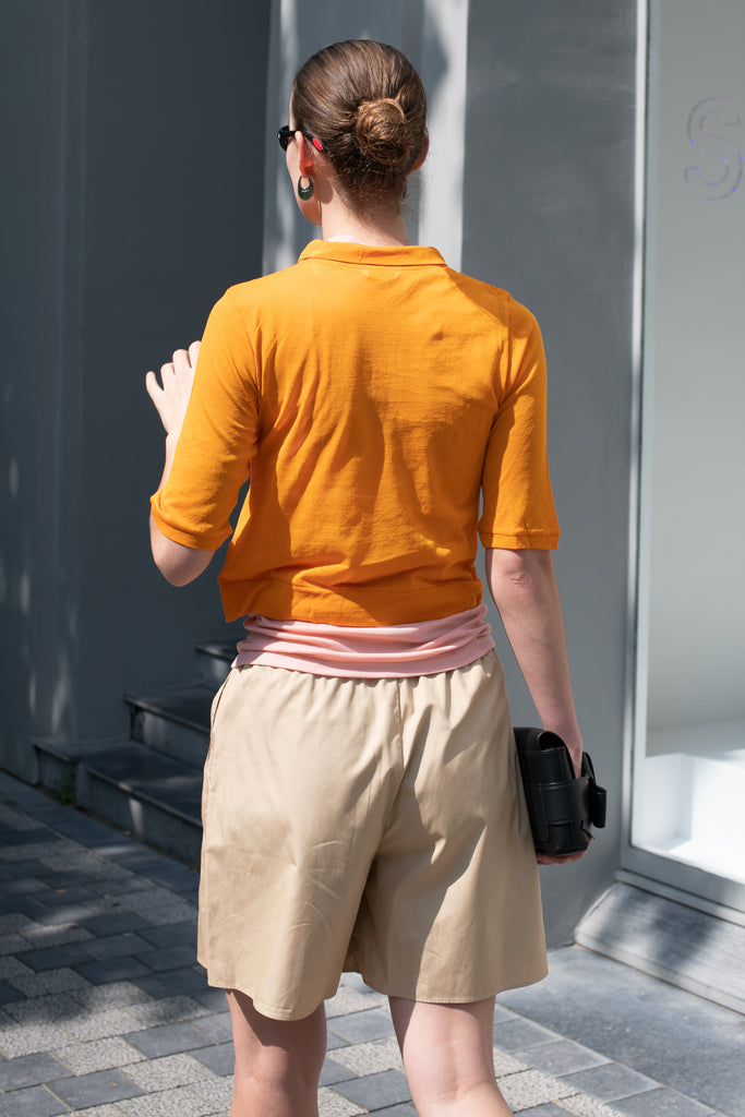 The Gauze Polo by Auralee is a cropped polo top in a vibrant orange sheer cotton jersey