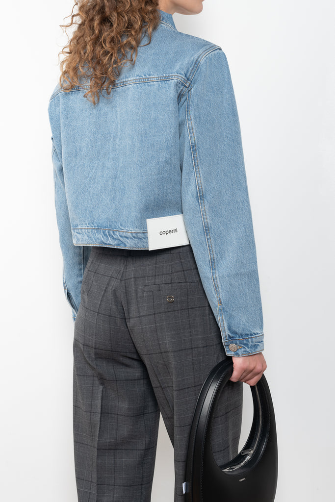 The Workwear Denim Jacket by Coperni is a cropped denim jacket with a zip closure and minimal details