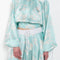 The Tracy Silk Blouse by Julie Kegels is a silk wrap top in aqua with a Hawaïan floral print and contrasting cuffs